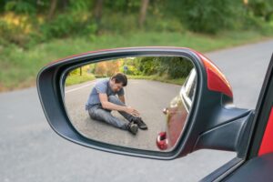 Pedestrian sitting injured on road reflected in car side mirror after hit-and-run accident scene
