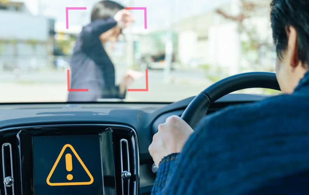 Driver’s view of pedestrian crossing suddenly with warning alert on dashboard illustrating dart-out defense in pedestrian accident case