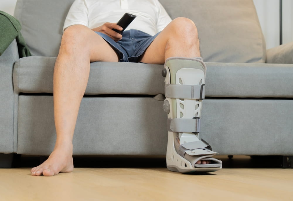 Person wearing a medical walking boot while seated on a couch recovering from a lower leg injury