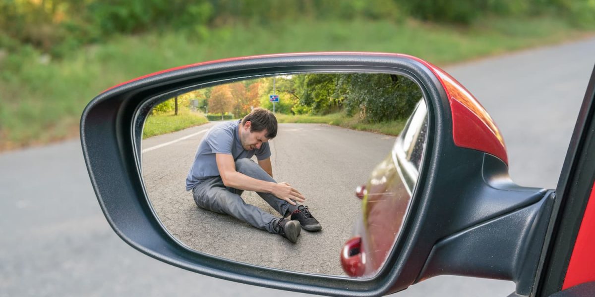 Pedestrian sitting injured on road reflected in car side mirror after hit-and-run accident scene