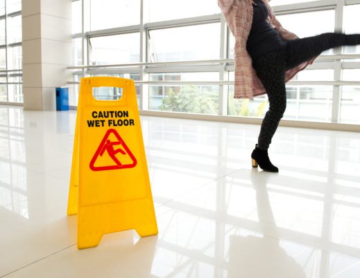 woman slipping near a yellow caution wet floor sign in a building lobby